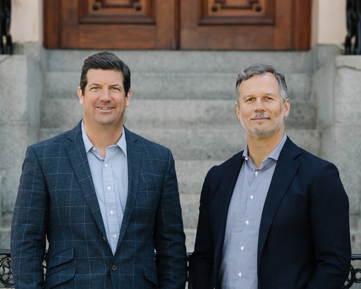 A professional photo of John and Mike outside with stairs and a door behind them